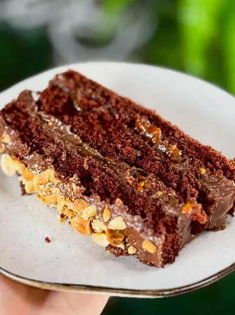 Fatia de bolo de chocolate com recheio cremoso e amendoim crocante na lateral